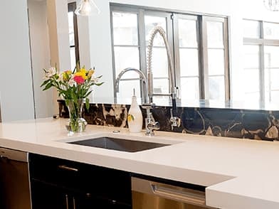 Kitchen island with a cream solid countertop, undermount sink and a vase of flowers