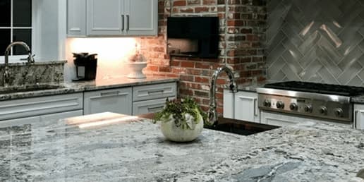 Kitchen with a granite island, a brick wall and a herringbone tile backsplash behind the range